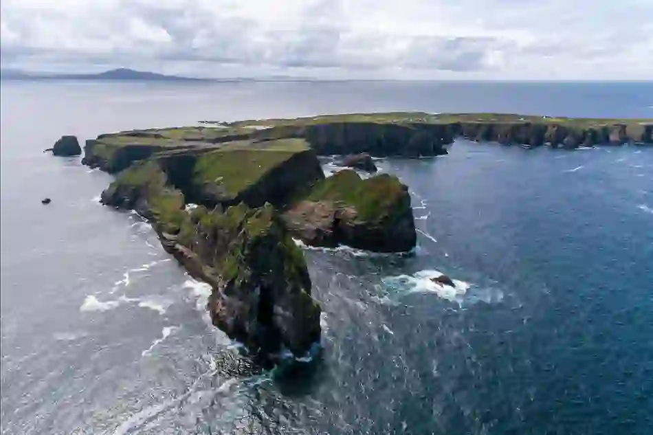 Aerial view of Tory Island’s dramatic cliffs and rocky coastline, with scattered houses visible on the island’s plateau.