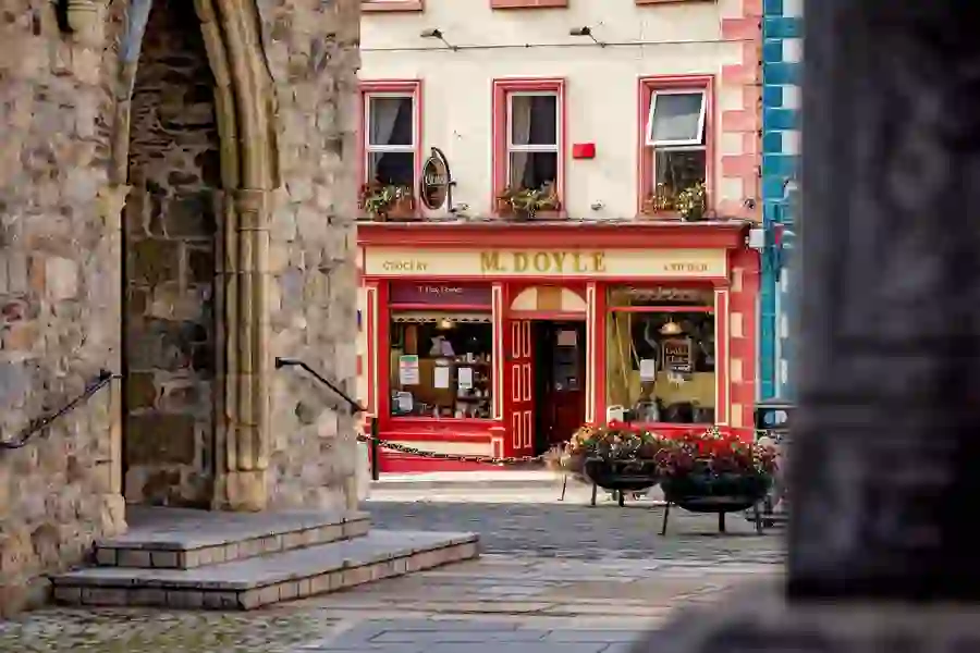View through a stone archway toward a traditional red-and-cream shopfront in Graiguenamanagh, County Kilkenny.