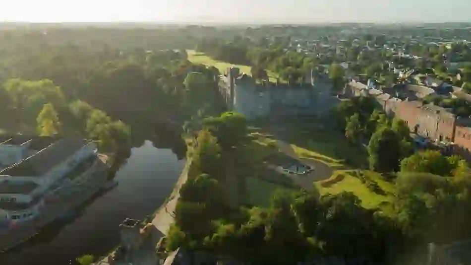 Aerial view of Kilkenny Castle surrounded by gardens and the city in soft morning light.