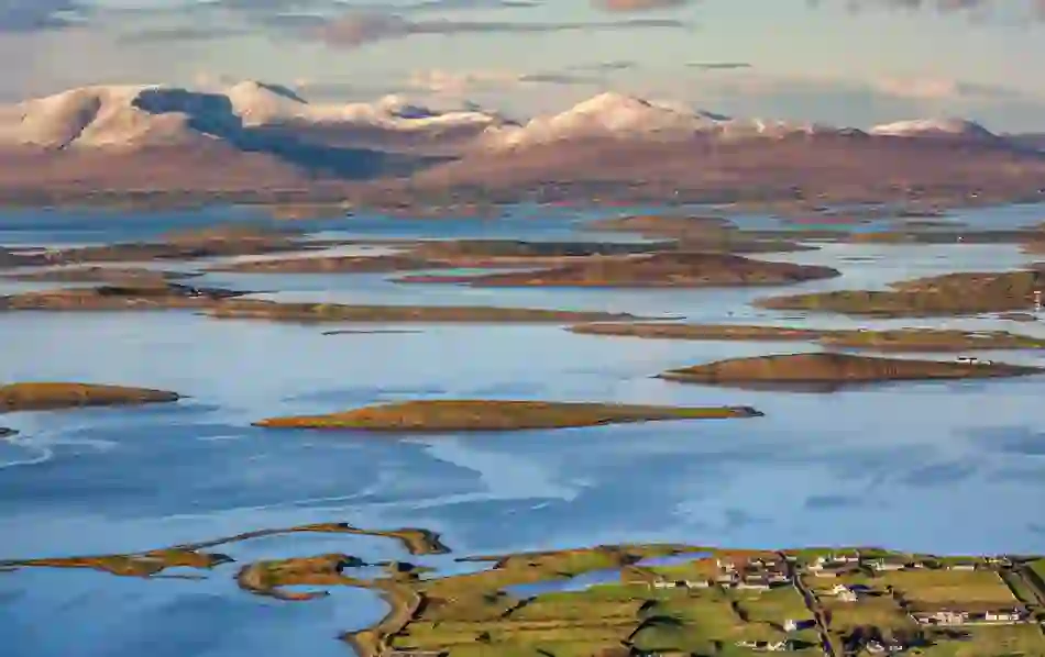 Scattered low-lying islands in Clew Bay with snow-capped mountains rising in the distance in County Mayo.