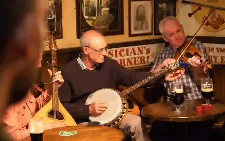 Traditional musicians play banjo and fiddle in a cosy pub with pints of stout on the table.