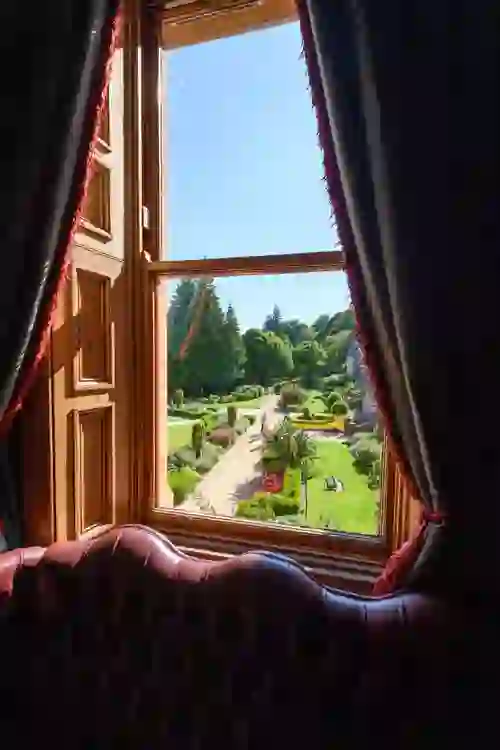 Window view from Belfast Castle interior framing manicured gardens with walking paths and flower beds.