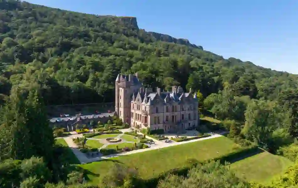 Historic Belfast Castle surrounded by trees at Cave Hill Country Park under clear summer sky.
