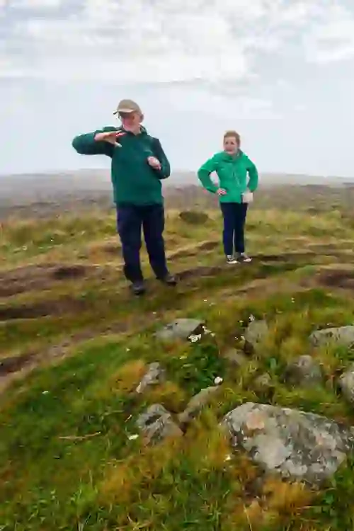 Walking guide explaining Cave Hill history to visitor standing beside grassy ridge.