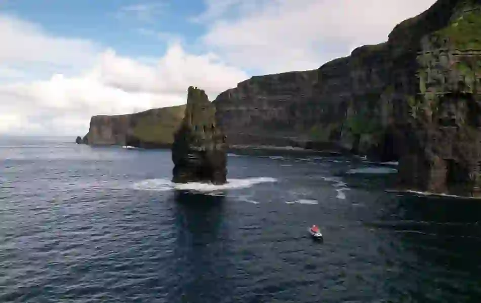 Boat sailing near the Cliffs of Moher in County Clare with sea stack Branaunmore rising dramatically from Atlantic waves.