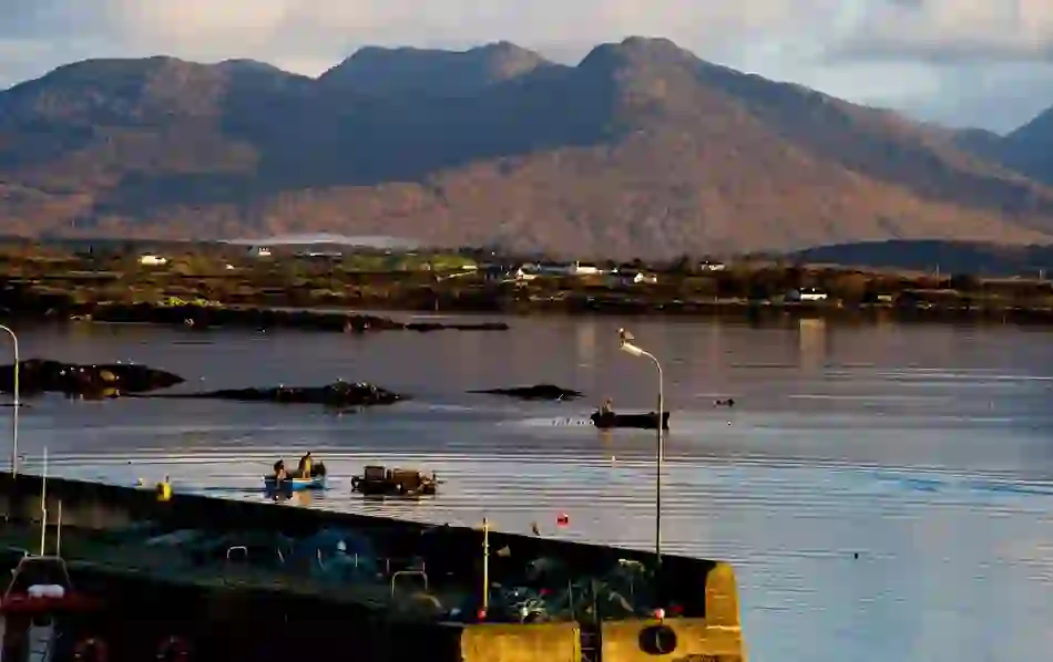 Roundstone Harbour in Galway with fishing boats and nets, set against Twelve Bens mountain range in evening light.