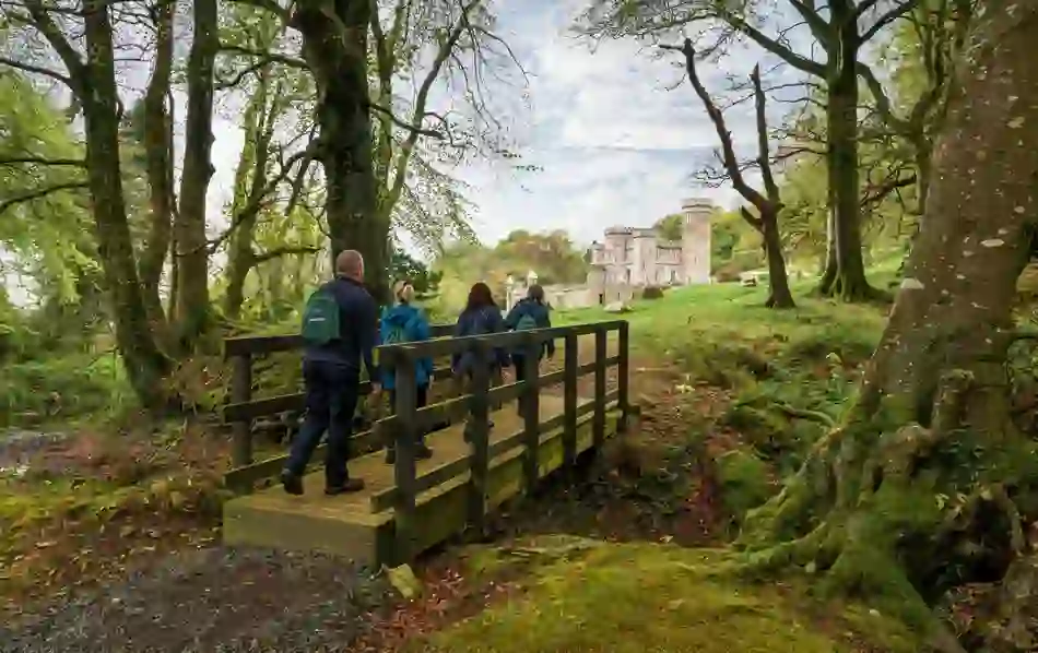 Group of walkers crossing wooden bridge in forest towards stone Killeavy Castle in County Armagh.