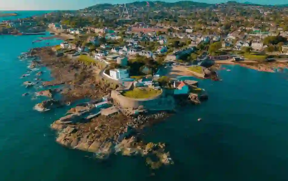 Aerial view of Dalkey coastline and Forty Foot bathing spot with swimmers on rocks in blue sea.