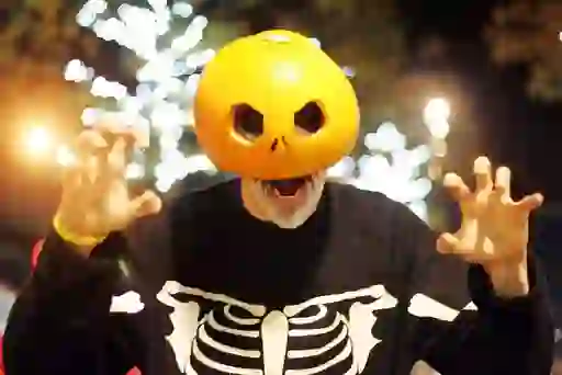 Person in a pumpkin head mask and skeleton costume celebrating at Derry Halloween.