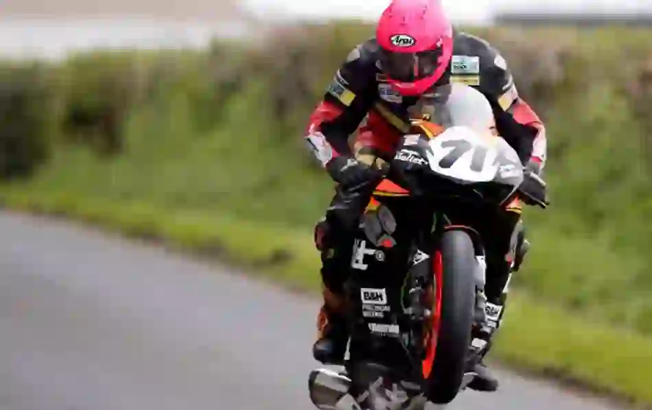 Motorcyclist wearing a pink helmet launching off the tarmac during a Tandragee 100 road race in County Armagh.