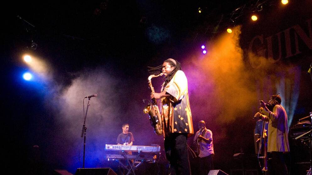 Saxophonist performs on smoke-filled stage at Cork Jazz Festival with band and vivid lighting.