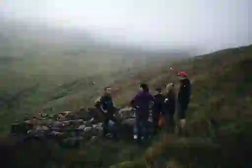 Group of hikers resting by a stone wall on misty slopes beneath Ben Bulben in County Sligo.