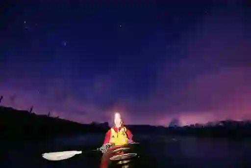Kayaker with headlamp paddling on the Roe River beneath a vivid night sky of stars.