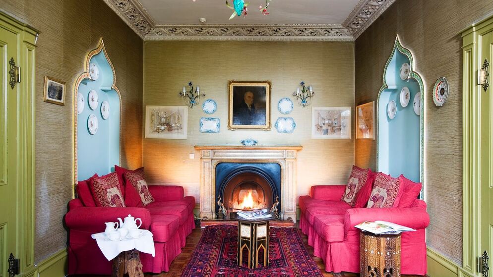 Period sitting room with red sofas, a lit fireplace and portrait in an ornate guesthouse in County Donegal.