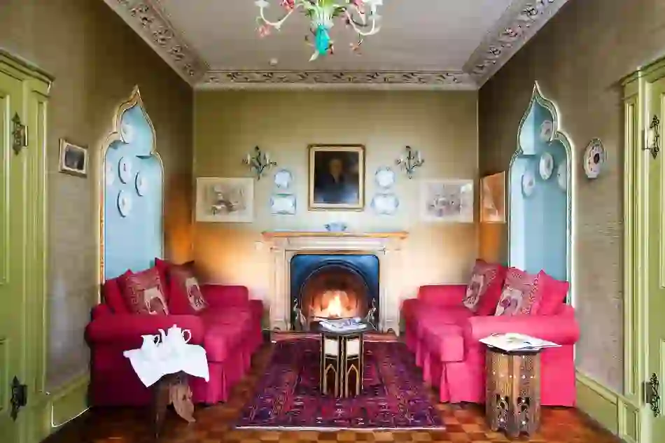 Period sitting room with red sofas, a lit fireplace and portrait in an ornate guesthouse in County Donegal.