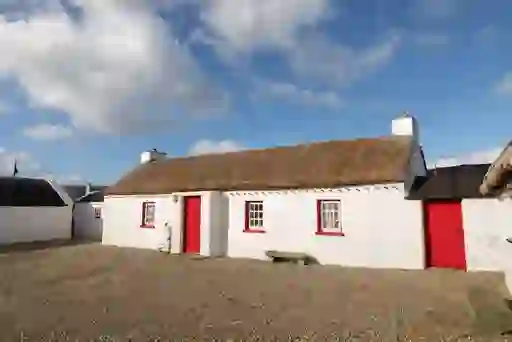 Whitewashed thatched cottage with red doors and windows on a gravel courtyard in County Donegal.