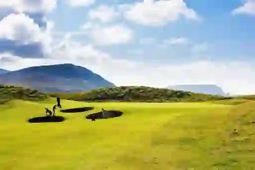 Golfers play near deep bunkers on a green with mountain and coastal views at Ballyliffin Golf Course, Donegal.
