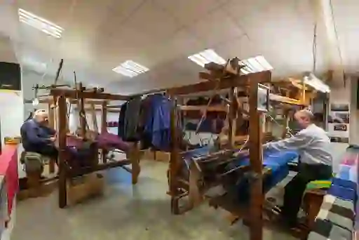 Two craftsmen weave at wooden looms inside Triona Donegal Tweed Visitor Centre in Ardara, showcasing traditional textile work.