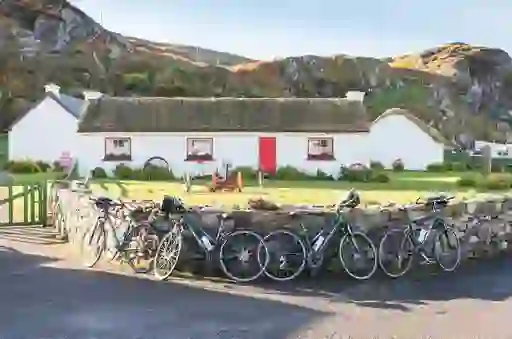 Bicycles lean against a stone wall in front of the traditional thatched cottages of Glencolmcille Folk Village, Donegal.