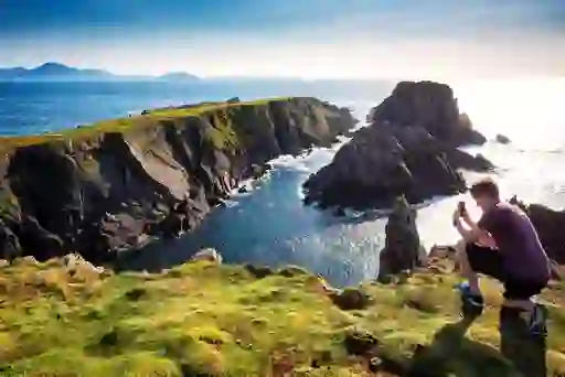 Person kneels with a camera at Malin Head, Ireland’s northernmost point, capturing the rugged coastal cliffs and ocean.