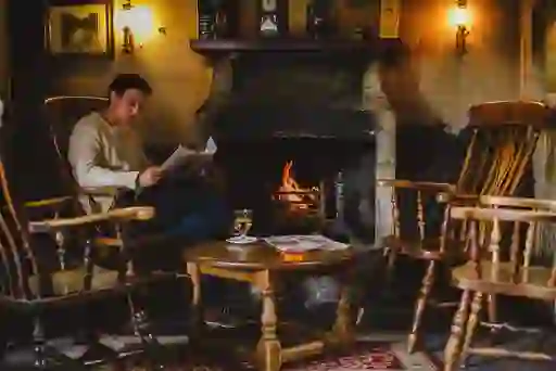 Man reading by a glowing fire with a drink in The Bushmills Inn, County Antrim.