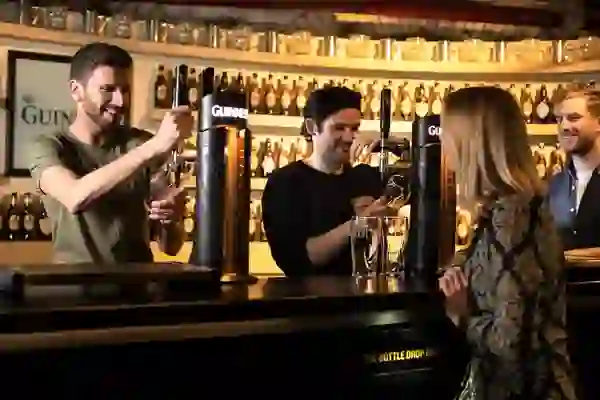 Bartenders pour pints of Guinness for visitors at The Bottle Drop Bar in Dublin.