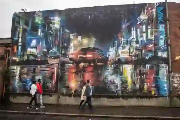 People walk past a vibrant city mural depicting neon-lit streets and cars in Belfast on a street art tour.