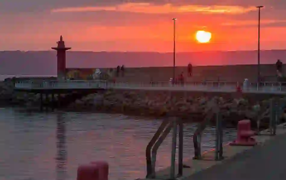 Sunset view at a coastal pier with people and dogs walking along the breakwater in County Down.