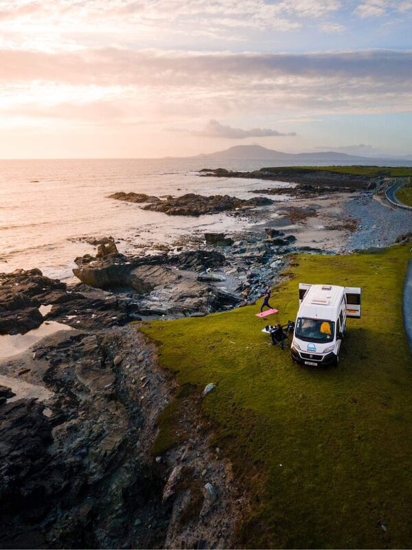 A campervan parked on a grassy cliff by the Atlantic on Fahy Beach in County Mayo overlooking a rugged shoreline at sunset.
