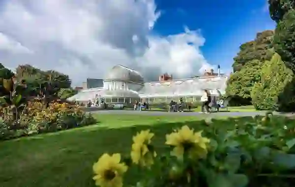 Palm House glasshouse in Belfast Botanic Gardens surrounded by lawns, flowers and visitors.