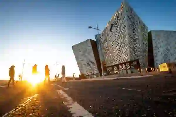 People walking past Titanic Belfast at sunrise in the Titanic Quarter.