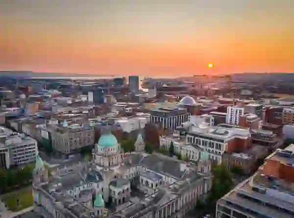 Aerial view of Belfast City Hall and the city skyline at sunset with Belfast Lough beyond.