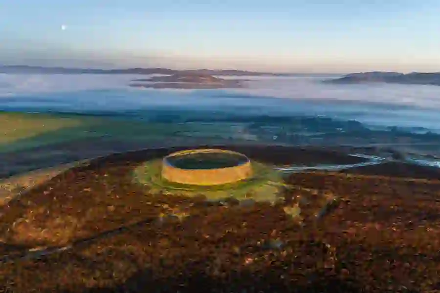 Aerial view of An Grianán of Aileach ring fort at sunrise, surrounded by misty hills in County Donegal.