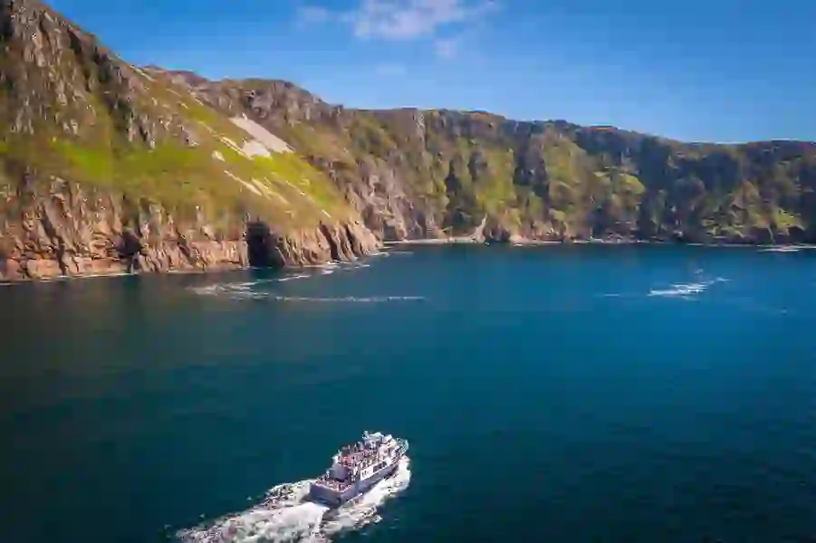 Tour boat cruising beneath the towering sea cliffs of Slieve League in County Donegal on a clear summer day.