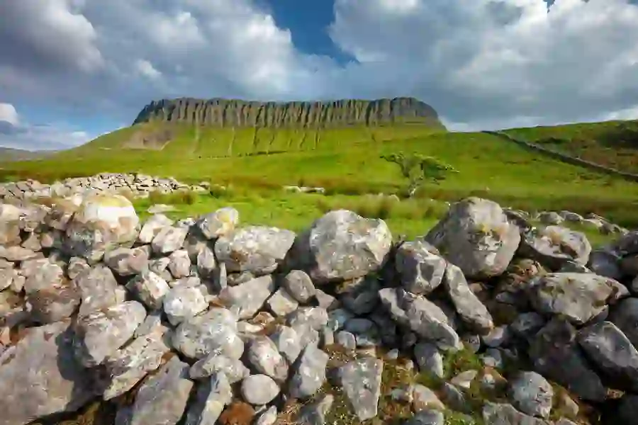 Ben Bulben mountain in County Sligo rising above green fields and a traditional dry stone wall under a dramatic sky.