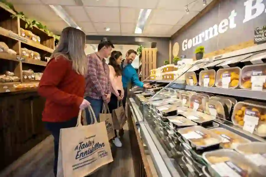 Shoppers with tote bags browse fresh baked goods and deli produce inside Gourmet Grocer, Enniskillen.