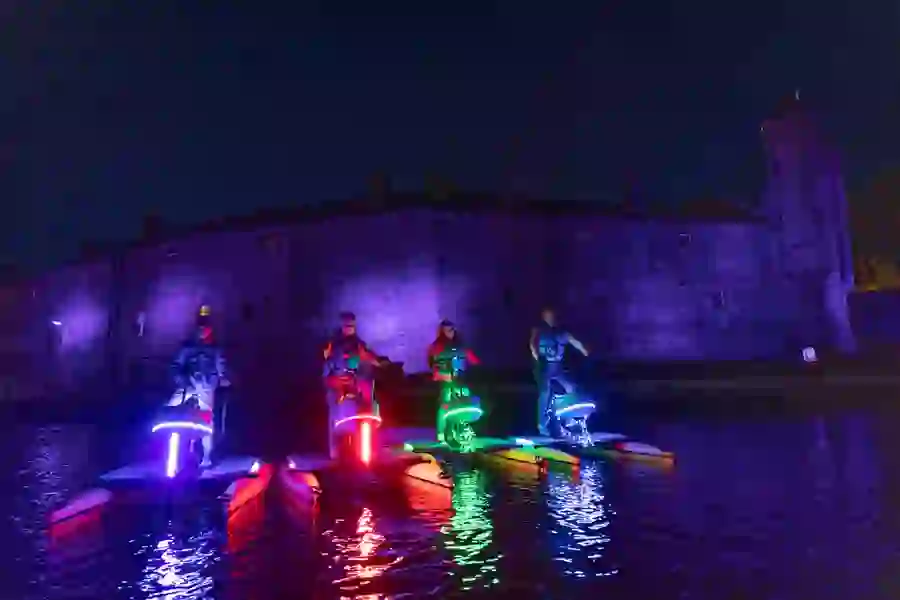 Group on illuminated water bikes with glowing neon lights in front of Enniskillen Castle lit purple at night.