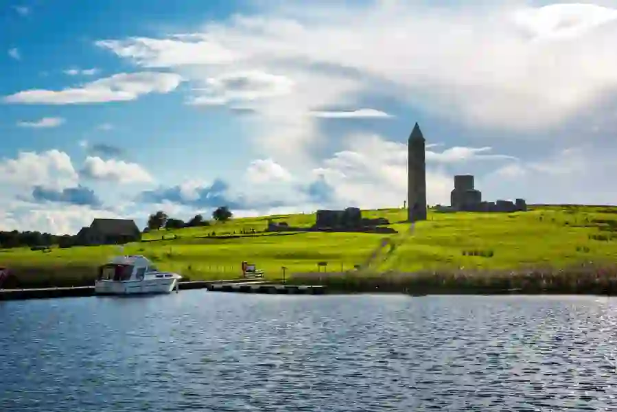 A boat docked at Devenish Island in County Fermanagh, with the ruins of a medieval round tower and church in the background.