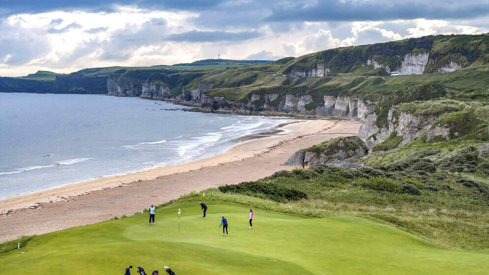 Golfers playing at Royal Portrush Golf Club with sea cliffs in the background.