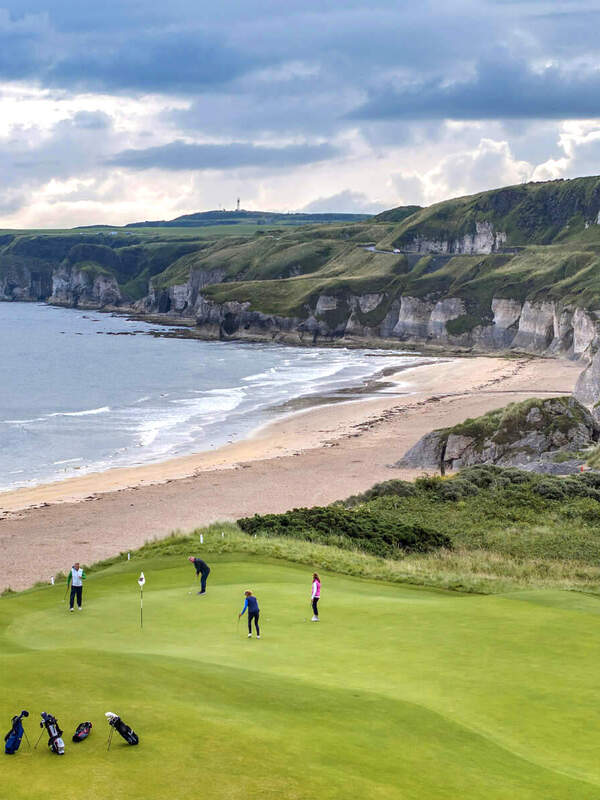 Golfers playing at Royal Portrush Golf Club with sea cliffs in the background.