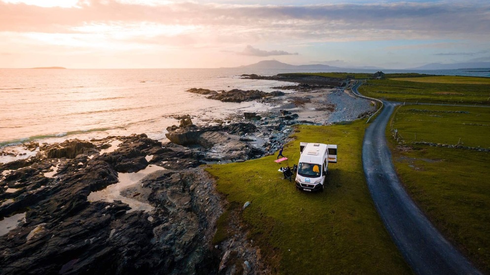 Coastal campervan parked by a rugged shoreline at sunset near the Wild Atlantic Way.