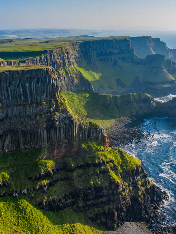 Basalt cliffs along the wild northern coast of Ireland at sunset, with waves crashing below.