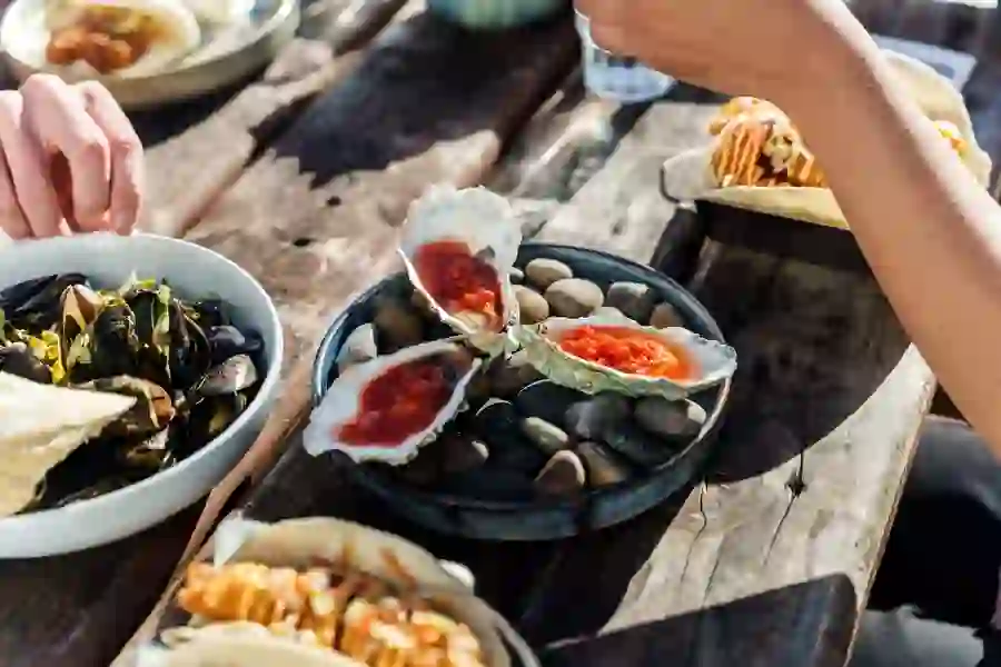 Fresh Irish oysters with red sauce served outdoors alongside mussels and tacos on a rustic table.