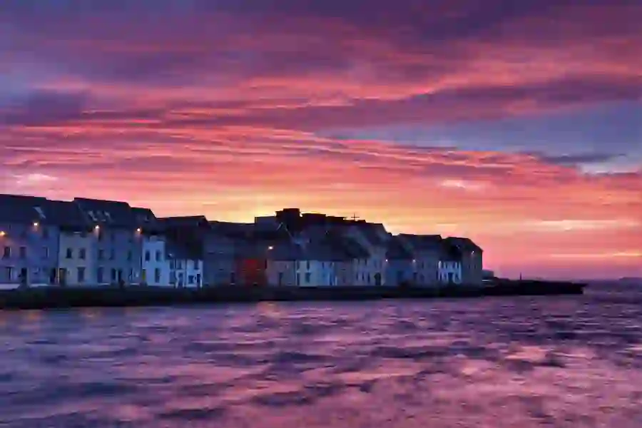 Vibrant sunset over terraced waterfront houses in The Claddagh, Galway city, beside rippling coastal water.