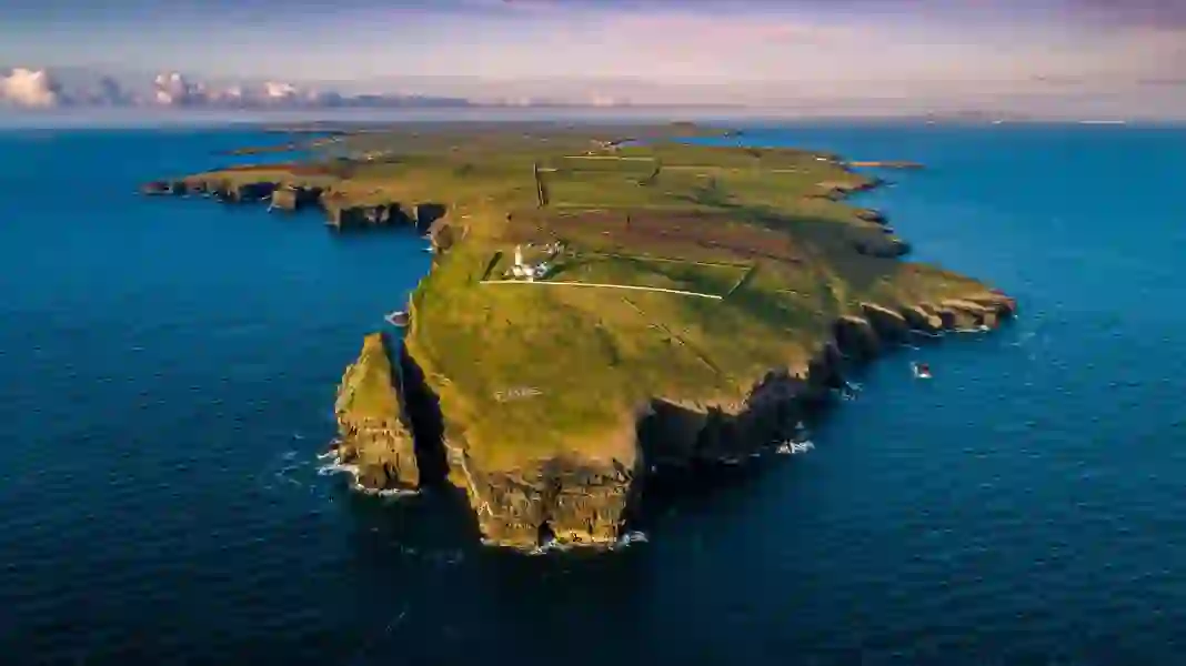 Aerial view of Loop Head Peninsula, County Clare, with cliffs, fields, and lighthouse surrounded by blue sea.