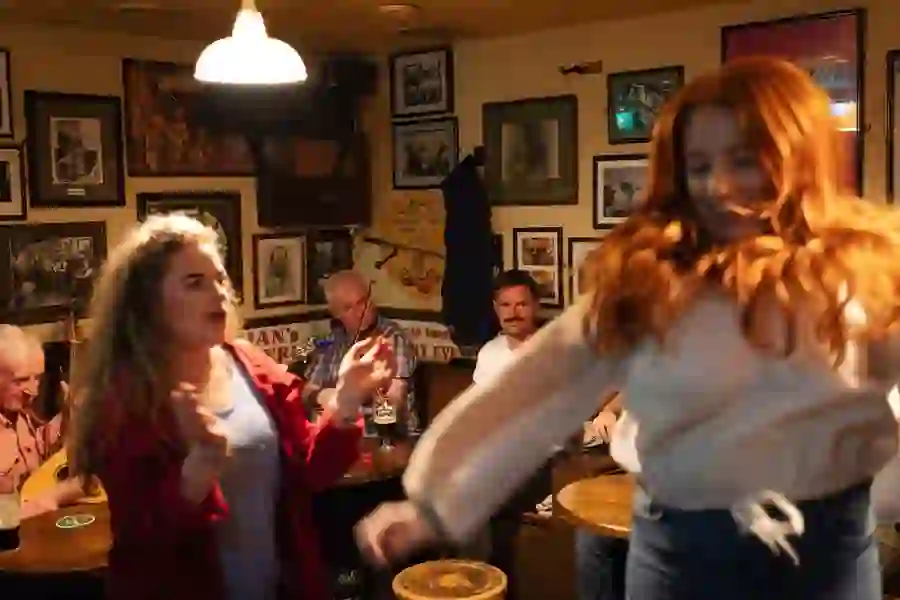 Two women dancing in Matt Molloy's lively pub with in Westport, Mayo, with people seated at tables in the background.