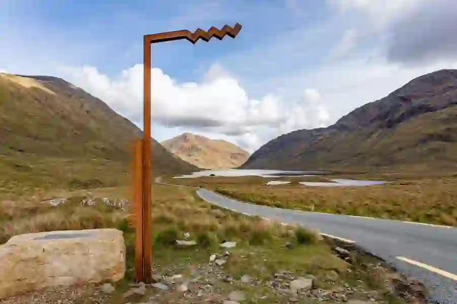 Scenic road curving through Mayo's rocky Doo Lough Valley with a Wild Atlantic Way marker sign.