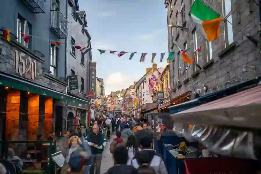 Colourful flags strung above a bustling pedestrian street in Galway city that is filled with people.
