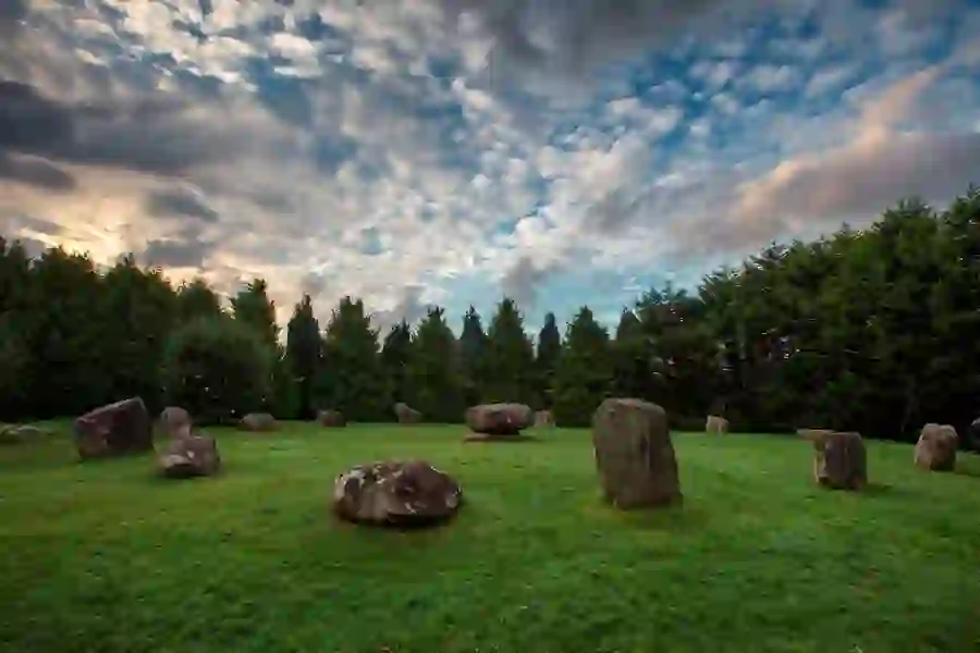 Ancient stone circle on grassy field surrounded by tall trees at dusk at Kenmare, County Kerry.