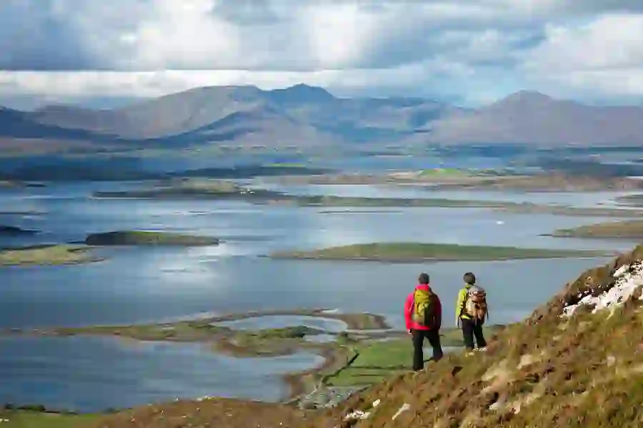 Two hikers overlooking Mayo's Clew Bay’s islands and calm waters from a hillside trail.